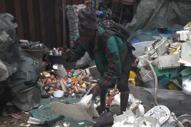 Un hombre está en medio de la basura recogiendo deshechos