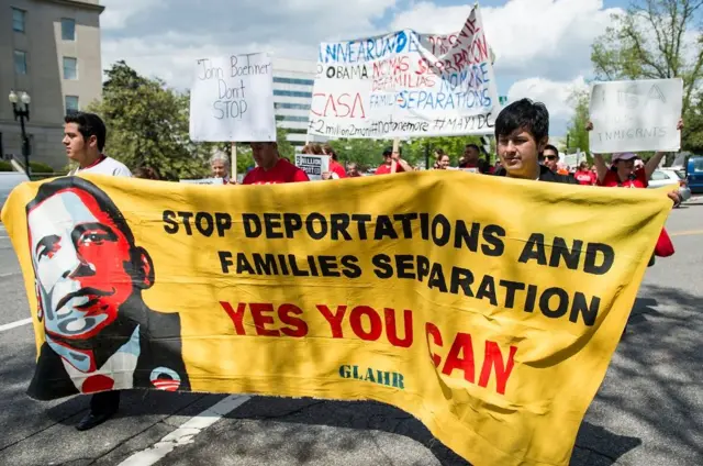 Manifestantes con una pancarta amarilla con el rostro de Barack Obama que dice: