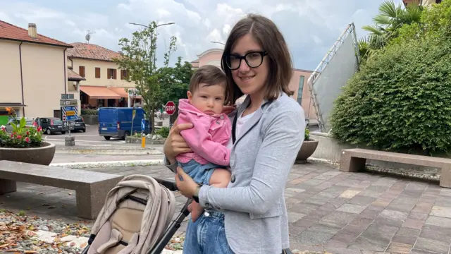 Valentina, una mujer de pelo oscuro y anteojos, sostiene a una bebé con suéter rosa