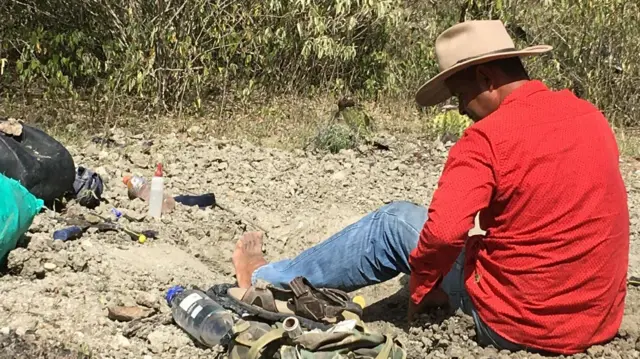 Un coleccionista de fósiles en Colombia, sentado en el piso, descalzo, con un sombrero y camisa roja  