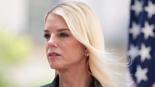 Pam Bondi mirando fuera de cámara con una bandera estadounidense de fondo