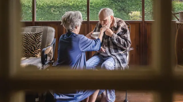 Una cuidadora alimenta a un anciano