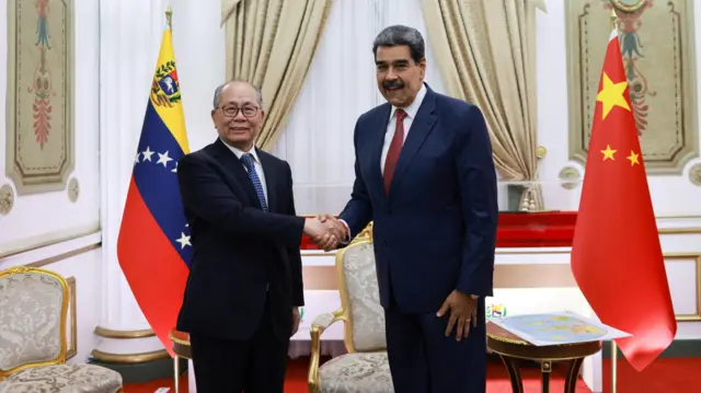  Nicolás Maduro (d) estrecha su mano al diplomático chino Qiu Xiaoqi (i), flanqueados ambos por las banderas de sus países, en el Palacio de MIraflores. 