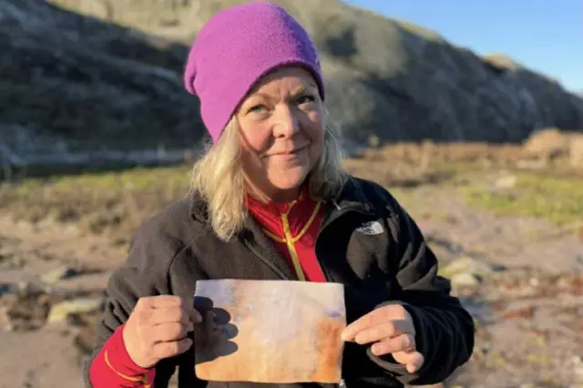 Una mujer -Asa Nilsson- sostiene una vieja y descolorida carta. Ella porta un gorro de lana violeta