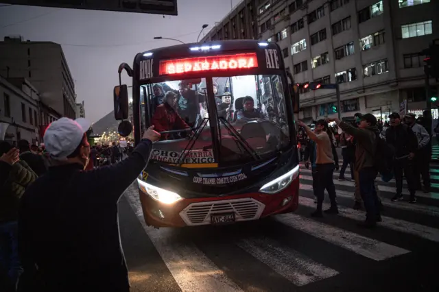 Un autobús maniobra en medio de una grupo de personas que gesticulan hacia él en el centro de Lima. 
