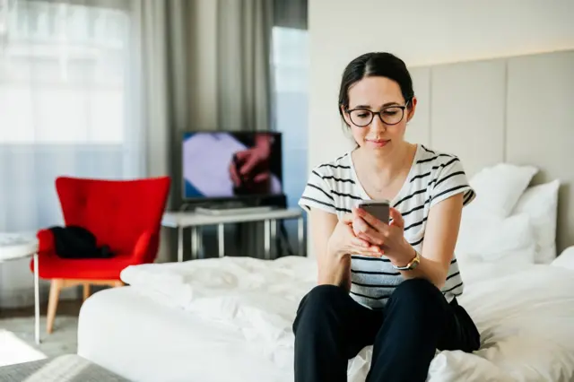 Mujer sostiene un celular sobre su cama.