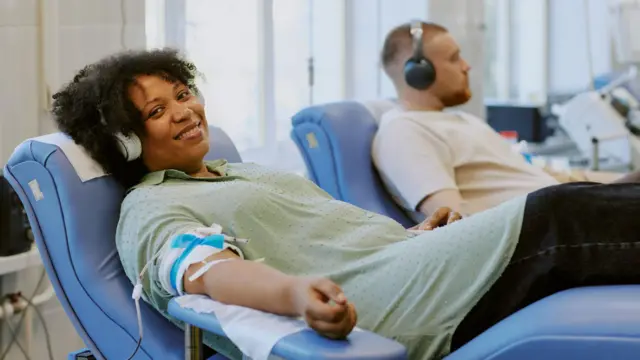 Una mujer afroamericana y un hombre caucásico donan sangre mientras se relajan en sillones reclinables.