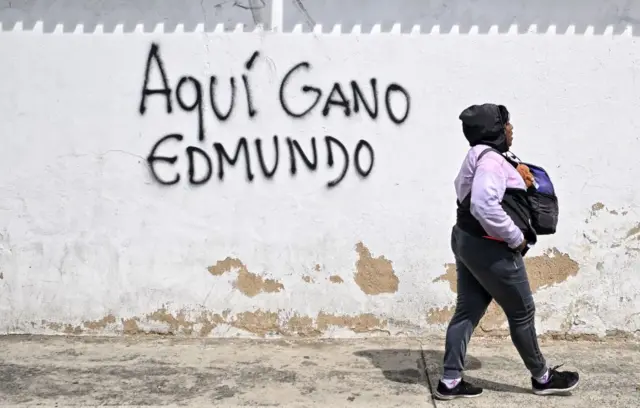Una mujer camina por una calle donde hay un grafiti que dice