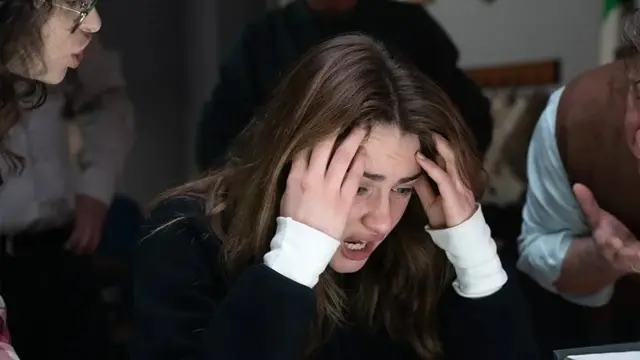 La actriz Grace Van Patten tiene las manos en las sienes en señal de desespero, mientras otros dos actores la interrogan, en la nueva serie de Disney.