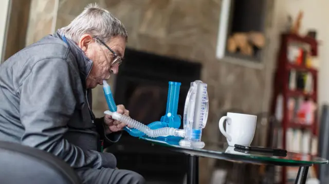 Un hombre mayor usando espirómetros desechables para ejercitar sus pulmones.