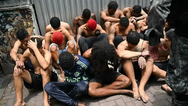 Delincuentes sentados en el piso con la cabeza gacha.