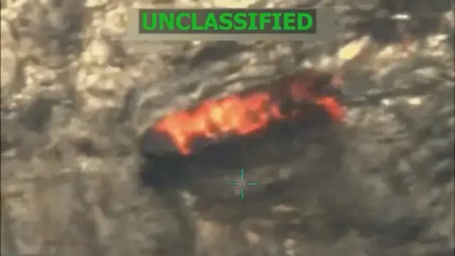 Una imagen de baja resolución muestra una lancha en llamas sobre el mar y, en letras verdes, la palabra en inglés 