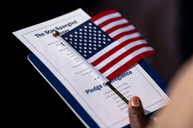 Una persona sostiene una pequeña bandera de EE.UU. y una copia con el himno y el juramento del país