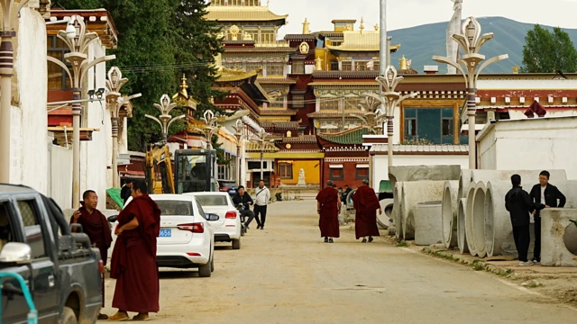 Monjes y otras personas en una carretera que conduce al monasterio de Kirti. Hay coches aparcados a ambos lados de la carretera.