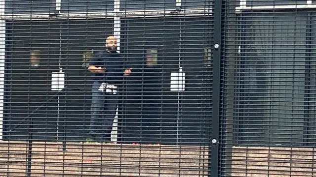 Un hombre calvo detrás de una verja.