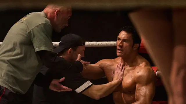 Johnson, interpretando a su personaje está en el ring. Está en una esquina mientras su entrenador le da consejos y el asistente revisa que su cuerpo esté bien.