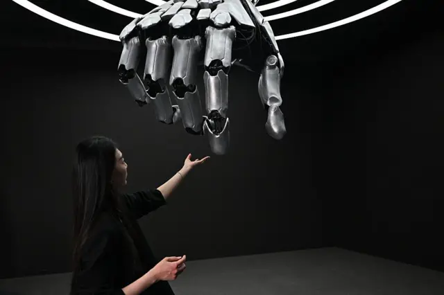 Una mujer toca una mano robótica durante una gira de prensa por el centro de exposiciones Robot World en Pekín el 17 de abril de 2025.