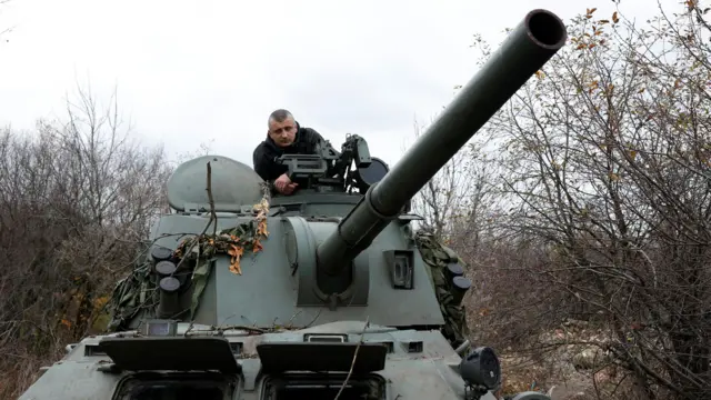 Un soldado observa desde un tanque gris en una zona boscosa. Los árboles están desnudos por el invierno y el cielo está gris. La torreta de un cañón apunta hacia la cámara. Soldados ucranianos se preparan para disparar un proyectil de un mortero autopropulsado 2C23 Nona-SVK en la línea del frente, desde un tanque capturado a soldados rusos en una batalla en Husarivka en marzo de 2022. Esta fotografía fue tomada en la región oriental de Donbás, en Bakhmut, el 4 de noviembre de 2022.