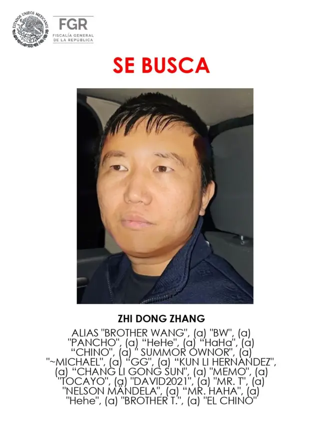 Nota de alerta emitida por la Fiscalía de Quintana Roo, México, donde se ve en el centro la foto de Zhi Dong Zhang en el interior de un auto, vestido con ropa deportiva, chaqueta azul oscura y camiseta negra. Encima, en letras rojas,