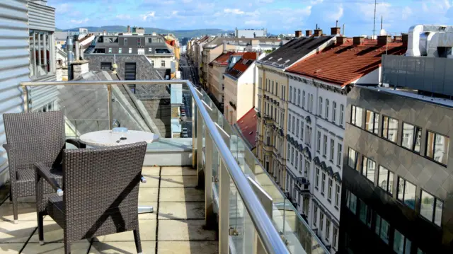 Sillas en una terraza al sol con la vista de la ciudad de fondo.