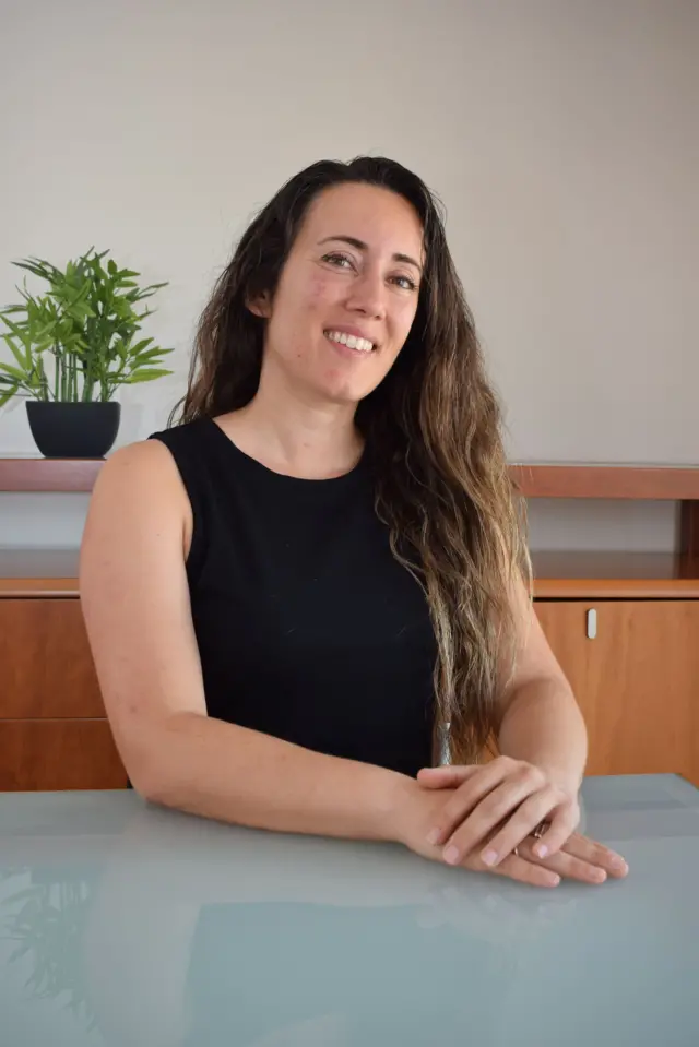 Plano medio de la experta Anna Grifols con una camiseta negra, las manos sobre una mesa de vidrio, sonriendo a la cámara