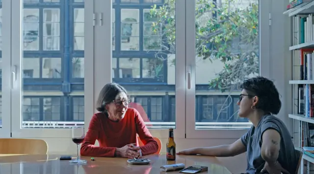 Marina Freixa, a la derecha, y su madre Mariona sentadas a una mesa con un gran ventanal detrás.