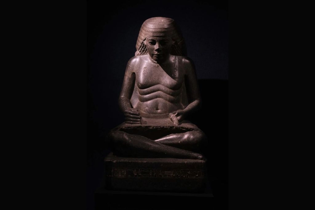 Una estatua de Amenhotep representado como escriba sentado, perteneciente a la dinastía XVIII (aproximadamente entre 1550 y 1292 a.C.), exhibida en el Museo de Luxor, Egipto. La postura inadecuada y la repetición constante de movimientos podrían haber provocado desgaste en sus articulaciones, columna vertebral y mandíbula