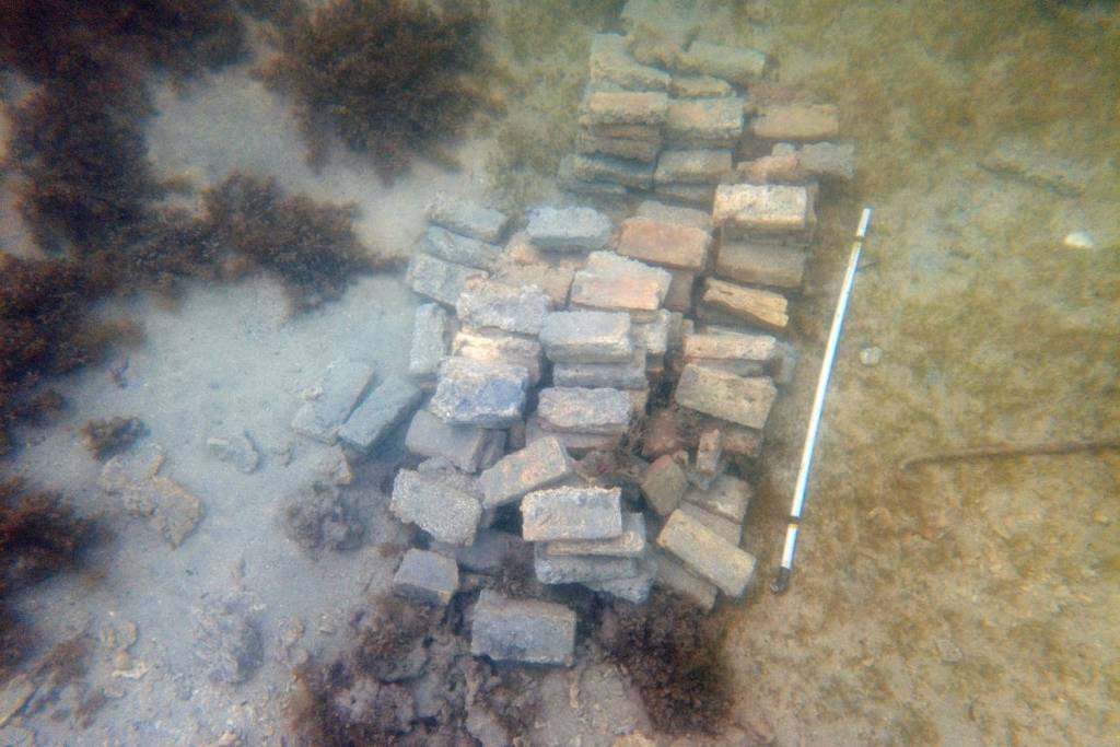 En la imagen se observa una excavación submarina donde sobresalen ladrillos y maderas del antiguo naufragio