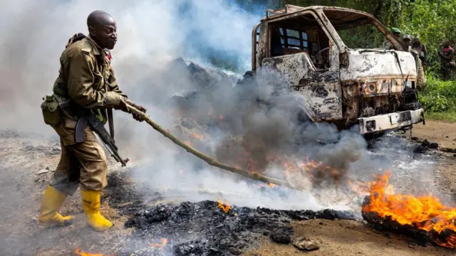 Soldados del ejército congoleño y tropas de la ONU inspeccionan el lugar de un ataque islamista en abril de 2021. Se ve a un bombero combatiendo las llamas.