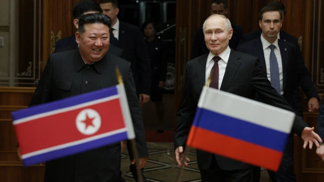 Kim Jong-un (izquierda) sonríe mientras camina junto a Vladimir Putin (derecha) frente a las banderas nacionales de Corea del Norte y Rusia.