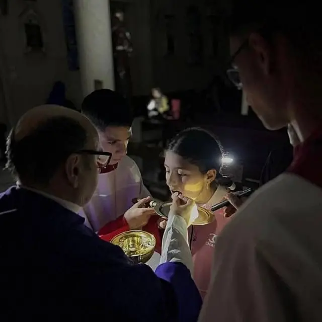 El padre Gabriel Romanelli dando la hostia a una adolescente mientras otros jóvenes iluminan con linternas