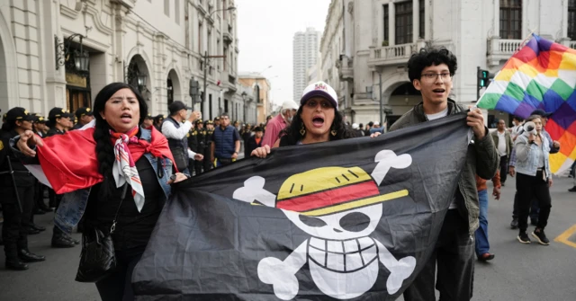 Tres manifestantes, dos mujeres y un hombre, sujetan una bandera negra con una calavera con dos tibias y un sombrero de la serie de animación 
