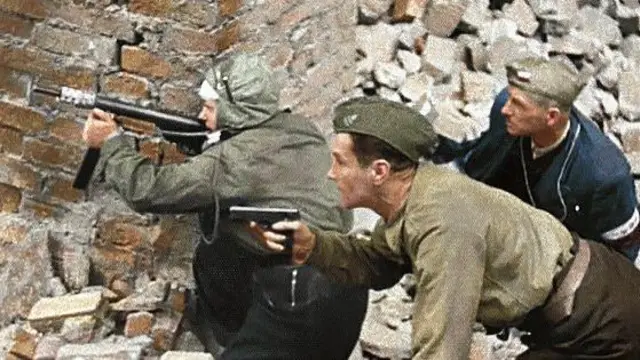 Una fotografía antigua, coloreada posteriormente, de tres combatientes de la resistencia polaca. Wanda está en el extremo izquierdo. Están agachados tras un muro apuntando con un arma. El suelo está cubierto de escombros.