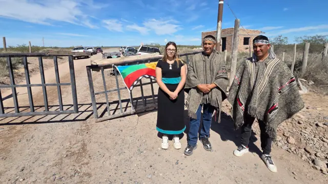 Tres personas paradas frente a una tranquera.
