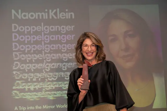 Naomi Klein con su premio y la portada del libro detrás