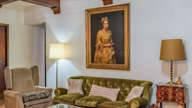 Una fotografía muestra una sala de estar con un sofá verde contra una pared blanca, flanqueado por dos lámparas. Un retrato cuelga en la pared detrás del sofá.