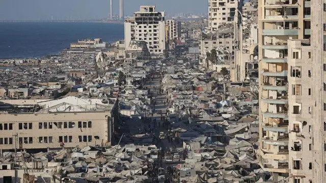 Imagen de una parte de la ciudad de Gaza tomada desde un dron o un edificio alto. Muestra una amplia zona repleta de tiendas de campaña a ambos lados de una carretera paralela al mar, con edificios dañados a ambos lados.