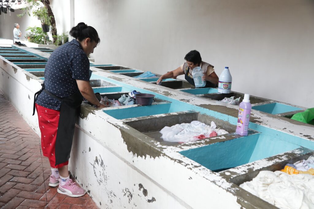 Dos señoras lavando tenis y ropa en los lavaderos públicos.