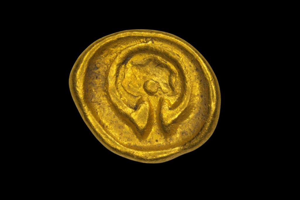 En el reverso de la moneda se aprecian un torques abierto, una estrella de cinco puntas y una pequeña esfera, elementos típicos del simbolismo celta